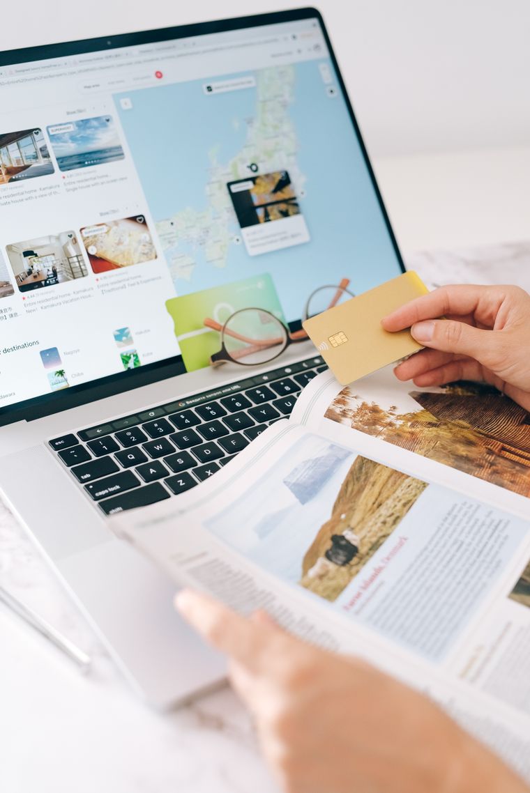 Hand holding a credit card beside a laptop during online travel planning