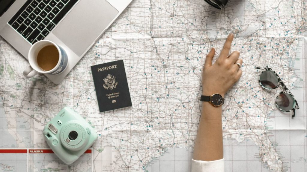 Hand pointing to a route on a map beside a laptop and travel essentials